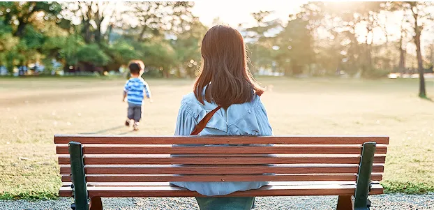 女性がベンチに座って子どもの後ろ姿を見守る様子